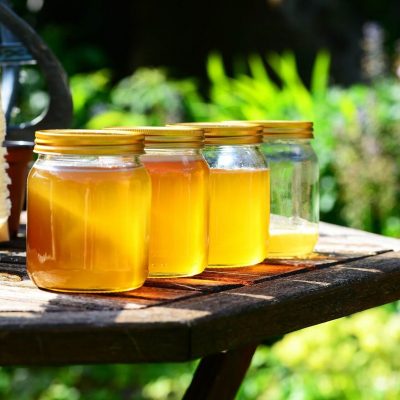 Four jars of honey sitting out in the sun.